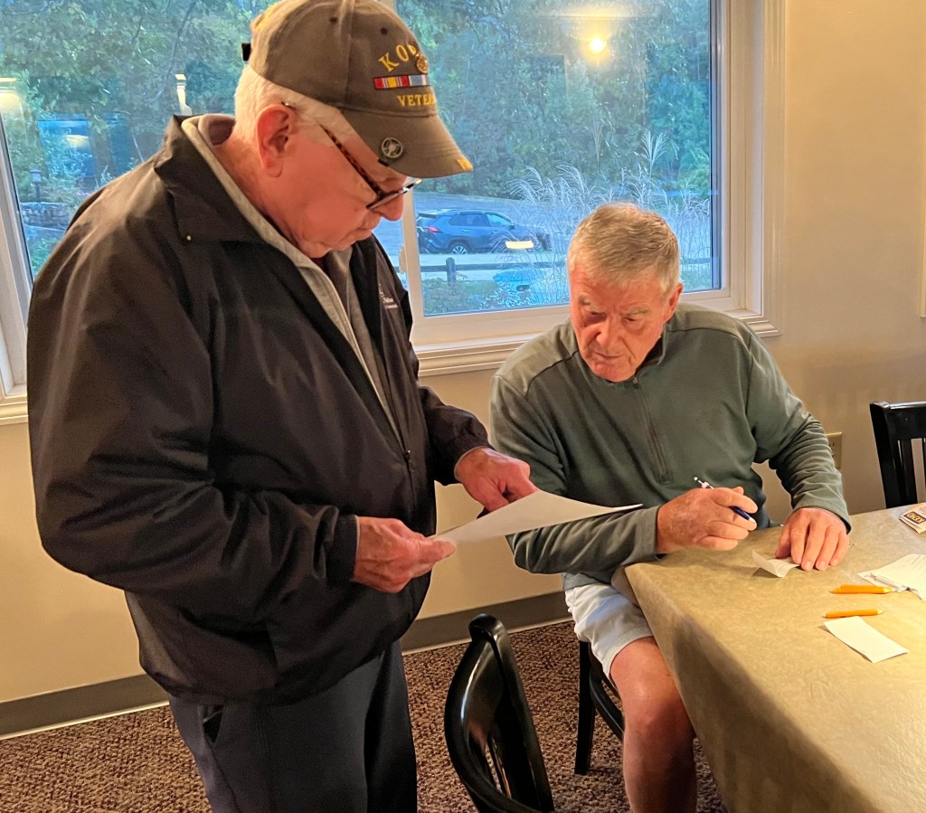 Two men engaged in conversation at a table, one holding a paper while the other takes notes.